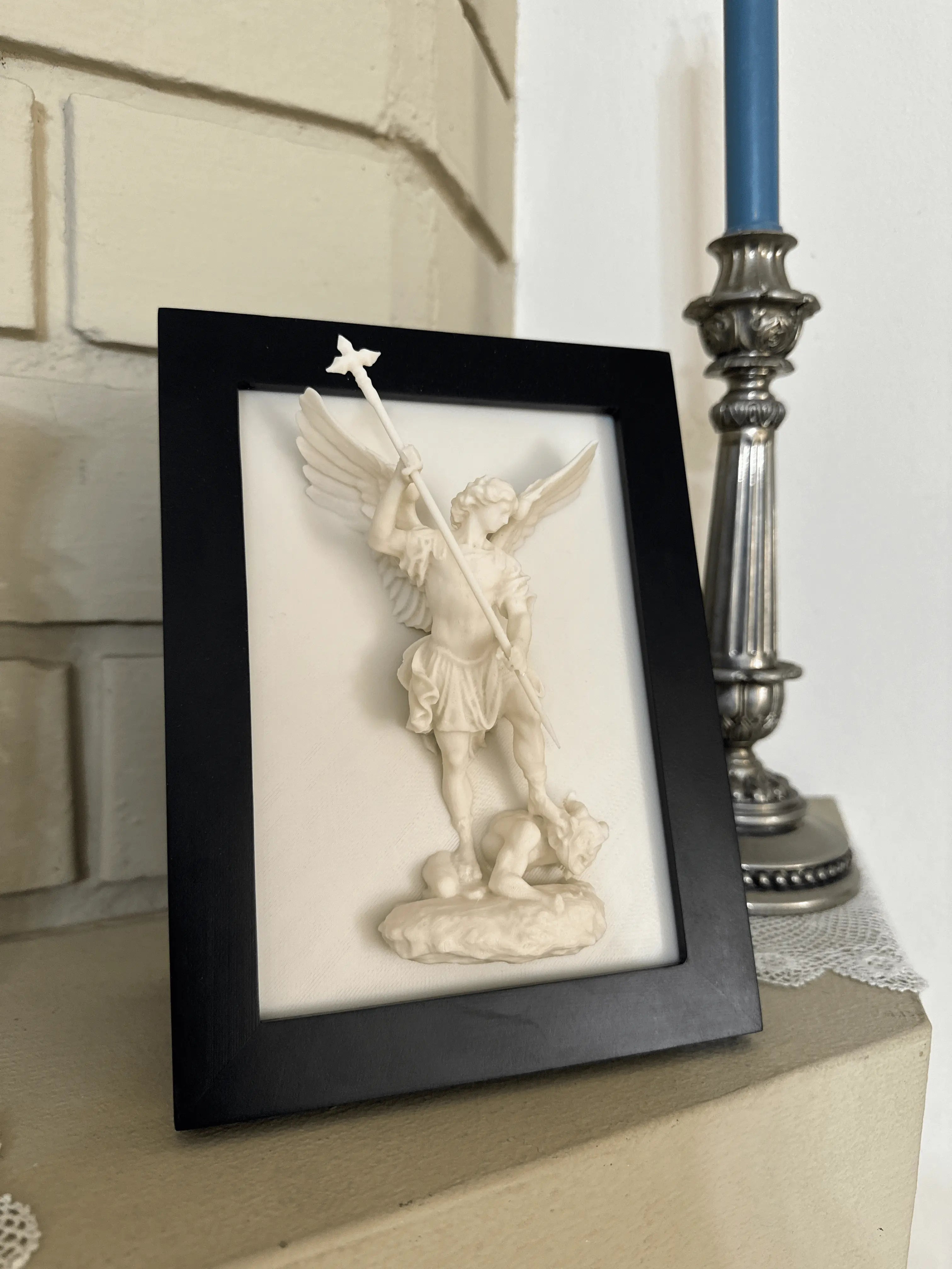 Framed statue of an angel on a mantel.